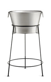 A large, round, TableCraft Products stainless steel tub sits on a black, tall, tripod-style metal stand with thin legs and a circular support. The tub has side handles and is perfect as a beverage tub set for holding ice drinks. Background is white.