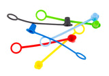 Five colorful tethered caps with flexible straps—red, yellow, blue, green, and black—are scattered in a pile on a white background. Each cap has a loop and a plug to cover and protect small cylindrical openings. Dishwasher safe for easy cleaning.