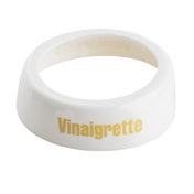 A white, circular, slightly angled ceramic ring with “Vinaigrette” printed in yellow on the side, this Dispenser ID Collar from TableCraft Products features a smooth surface and a hollow center.