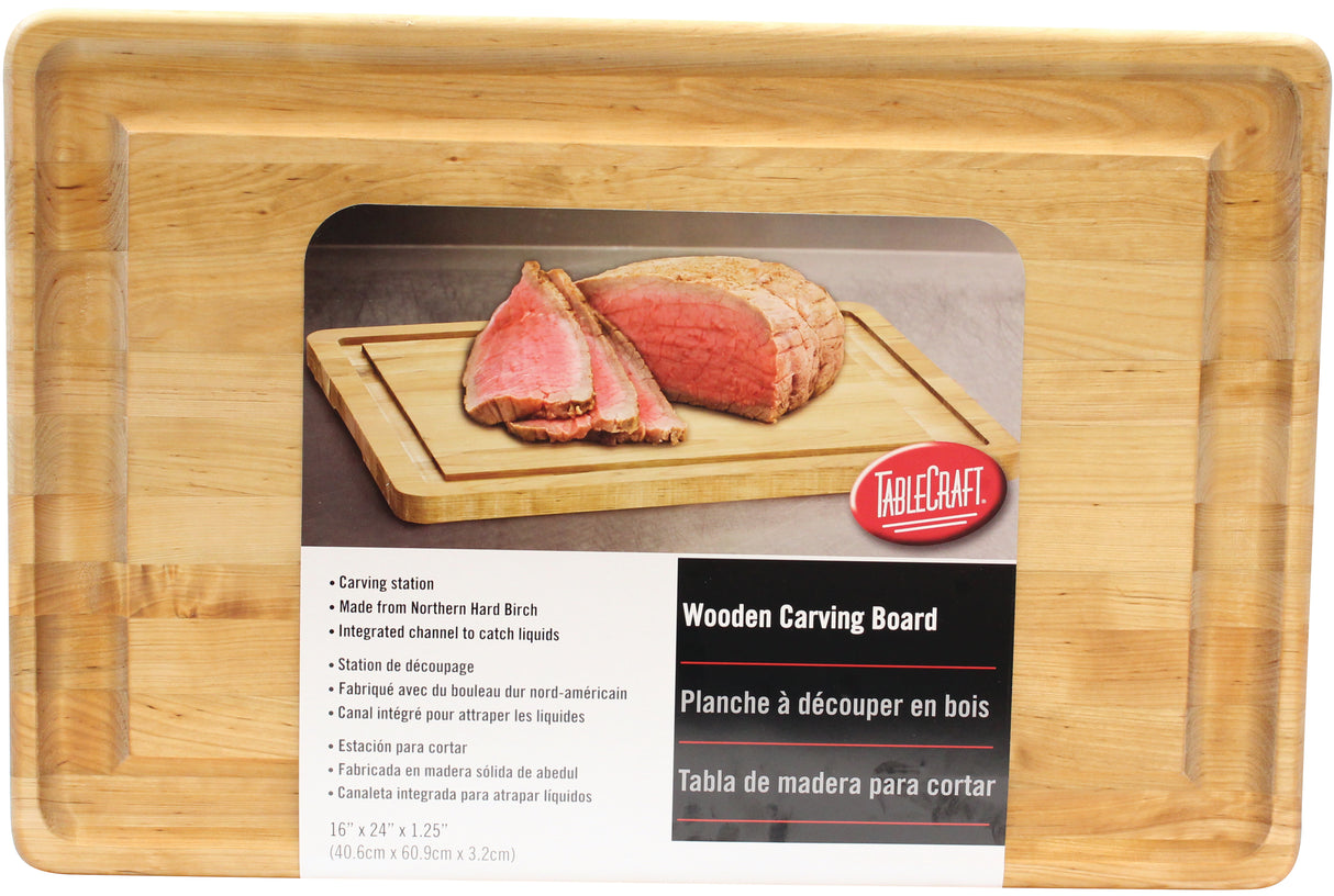A rectangular TableCraft carving board with a groove along the edge is shown. The label displays sliced roast beef and includes product info in English, French, and Spanish. Label reads: Wooden Carving Board, 16 x 24 x 1.25.