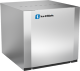 A stainless steel, box-shaped Modular Cube Ice Maker labeled Ice-O-Matic. The front panel is smooth with a blue and white logo. The unit, featuring a water-cooled condenser, sits on small black feet and produces half-size cubes.