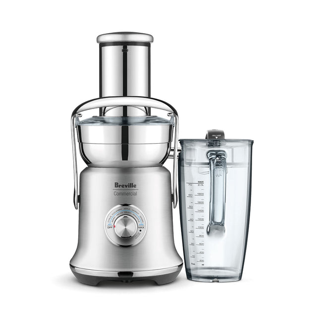A silver Breville centrifugal juicer with cold spin technology features a wide feed chute, transparent pulp container, and control dial. It sits beside a clear plastic juice pitcher with measurement markings on a plain white background.