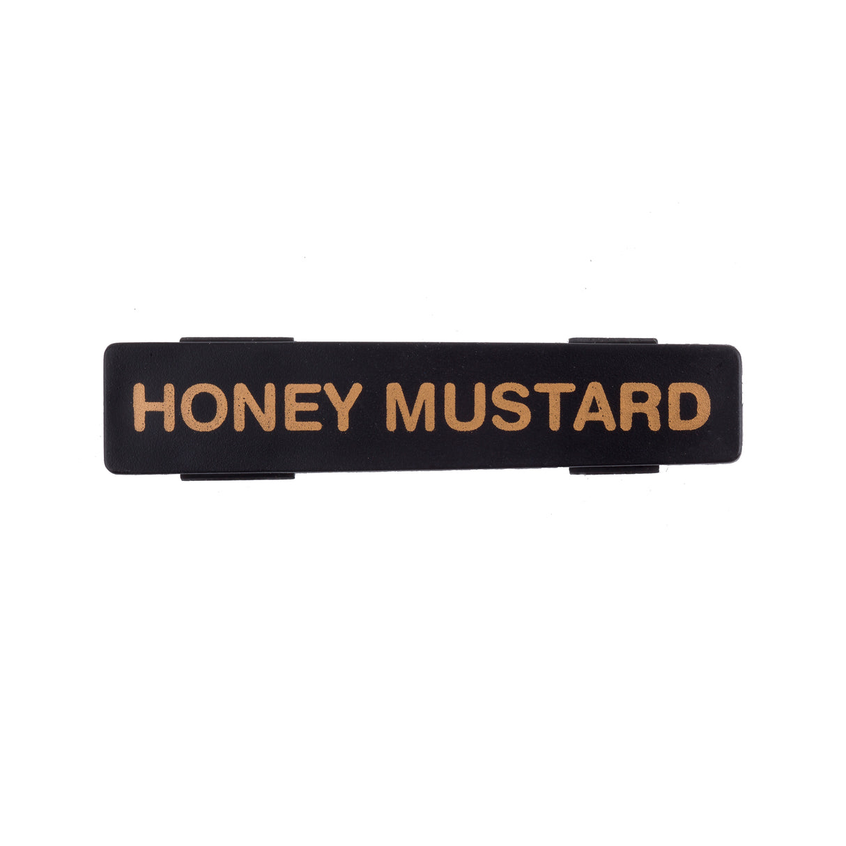 A rectangular black plastic TableCraft name tag with gold capital letters reading “HONEY MUSTARD.” The sign has two small clips on the back for attachment, and the background is white.