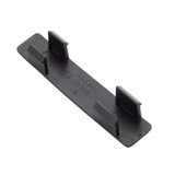 A rectangular black plastic clip with four upward-facing rectangular tabs—two on each long side—designed to secure a name tag or label. The surface features small embossed symbols and text, including arrows, letters, and numbers. Edges are smooth and slightly rounded.