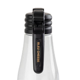 A clear salad dressing dispenser with a black flip-top lid is shown close up. The lid features a vertical name tag that reads BLEU CHEESE in gold uppercase letters. The white background keeps the focus on the bottle’s cap and label.
