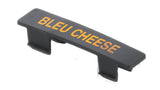 A black plastic name tag with two prongs underneath displays the words BLEU CHEESE in bold yellow capital letters. The label is photographed against a plain white background.