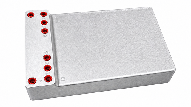 A rectangular, metallic device with a matte finish, featuring seven red circular ports labeled “1,” “2,” “3,” “S,” “C,” “N,” and “+” on its raised left section. The cold plate integrates stainless steel tubing from Micro Matic.