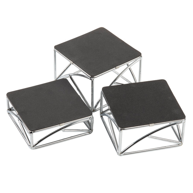 Three modern square display stands with black tops and chrome plated silver metal frames are arranged at different heights. The geometric, angular frames create a striking look as the riser set is grouped closely on a white background.