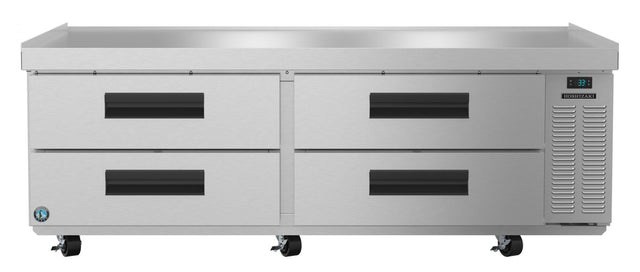 A large stainless steel refrigerator, designed as a low-profile refrigerated equipment stand, features four pull-out drawers, black handles, a digital temperature display on the right, ventilation panel, two front wheels, and a flat top surface against a white background.