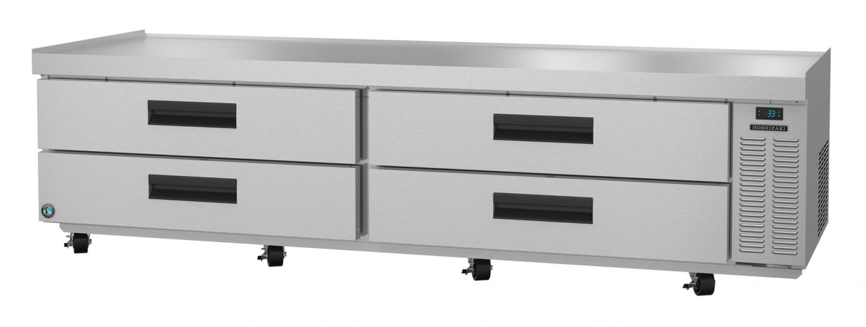 A large, stainless steel refrigerated stand with four black-handled pull-out drawers, ventilation grates on the right, a digital temperature display, and wheels for mobility. The flat top serves as a practical, modern low-profile equipment stand.