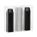 A clear acrylic countertop organizer holds three vertical stacks of disposable cups: two stacks of black plastic cups on the left and right, and one stack of translucent, textured plastic cups in the center. The holder is rectangular with open top and front.