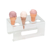 An acrylic clear ice cream cone holder with 6 holes displays three cones—two in light brown cones with pink ice cream and one in a waffle-style cone with white ice cream—while the other slots remain empty.