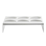 A rectangular, white TableCraft stand made from nylon coated cast aluminum with six oval-shaped depressions designed as a dressing template. Flat legs elevate it off the ground, creating a modern and minimalistic look.