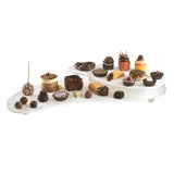 A white, three-tiered cast aluminum display stand holds assorted desserts—cupcakes, cake pops, truffles, mini cheesecakes, brownies, and chocolate-dipped treats—arranged neatly in rows on each tier against a plain background.