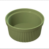 A green, round souffle bowl with a smooth interior and vertical ridges on the exterior. The ceramic dish has a glossy finish and is empty, viewed from a slight angle above, highlighting its depth and shape.