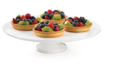 Four small fruit tarts sit on a Duracoat cast aluminum cake stand. Each tart features a golden crust topped with kiwi, blueberries, blackberries, and raspberries. The plain white background highlights the vibrant fruit and elegant presentation.