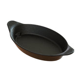 A black oval cast aluminum server with a brown outer surface, two textured handles for gripping, and a smooth, nonstick interior. The dish appears empty and is shown on a white background. It is also dishwasher safe.
