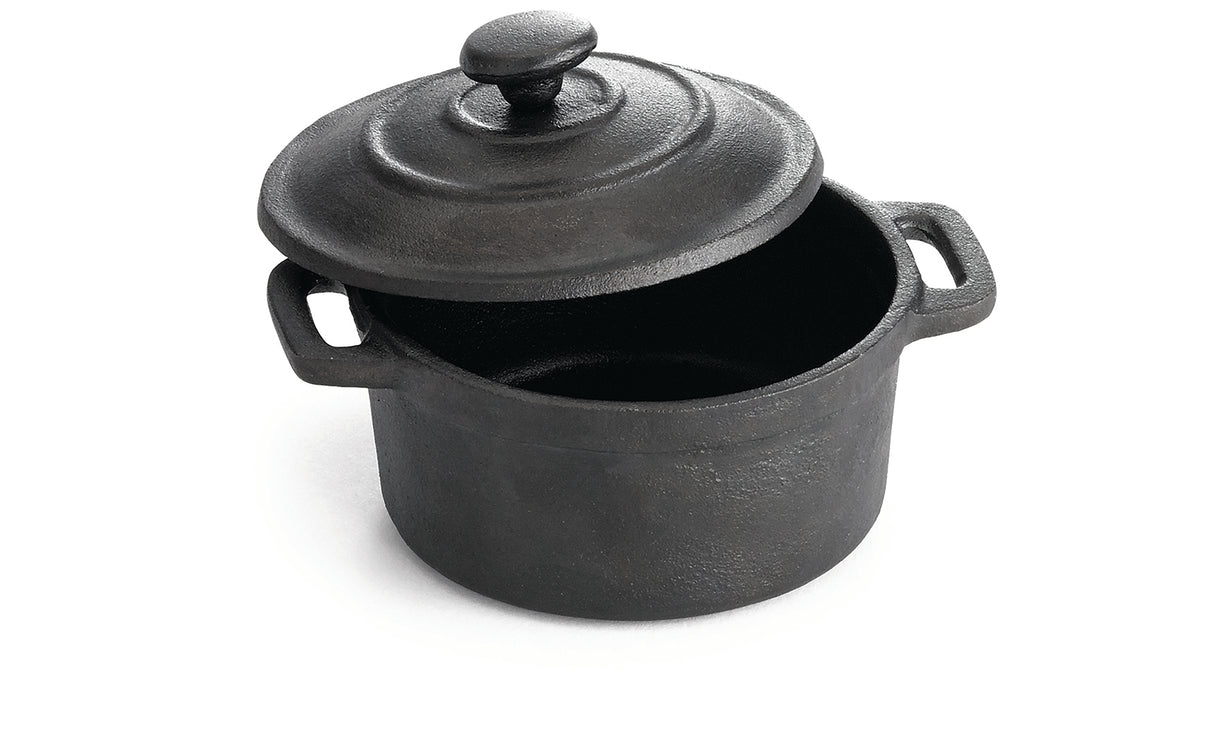 A black, round TableCraft cast iron mini casserole dish with handles on both sides and a matching lid, slightly tilted open, sits on a white background. The pot appears empty and has a textured, matte finish.