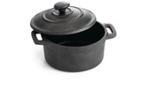 A black, round TableCraft cast iron mini casserole dish with handles on both sides and a matching lid, slightly tilted open, sits on a white background. The pot appears empty and has a textured, matte finish.