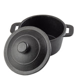 A black cast iron Dutch oven with a matching lid partially tilted off, revealing the empty interior. The pot has two side handles and a textured surface, resembling a TableCraft mini casserole dish, positioned on a white background.