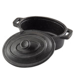 A black TableCraft cast iron oval dutch oven with two handles and a matching lid. The lid is slightly tilted off, resting against the pot, revealing the empty interior. The surface features a matte, textured finish.