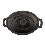 Overhead view of a black cast iron Dutch oven with a lid featuring concentric oval ridges and a central knob handle. The slightly worn surface hints at frequent use, while sturdy side handles evoke the charm of a classic TableCraft mini casserole dish.