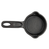 The TableCraft Mini Skillet is a small, round, black cast iron skillet with a handle featuring an oval hole. It has two small pouring spouts on opposite sides and a textured surface, shown against a white background.
