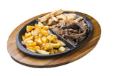 A divided black oval plate rests on an Acacia Underliner wood board, holding seasoned potato wedges, fried potato chunks, and strips of grilled beef in three separate sections. Each dish is neatly arranged against a white background.