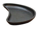 A black, kidney-shaped TableCraft cast iron plate with a shallow, smooth surface and gently curved edges is shown on a white background. Its unique organic form and indented side give this server an asymmetrical, modern appearance.