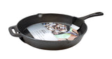 A black pre-seasoned cast iron skillet with a handle and side grip holds a product label featuring cooked shellfish. The label is partially tucked under the skillet’s rim, and the pan rests on a white background.