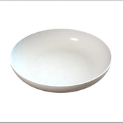 A plain, round, shallow white ceramic pasta bowl is centered on a white background, casting a soft shadow beneath it. The bowl has smooth, clean lines and a glossy surface, with a subtle reflection of light on its inner side.