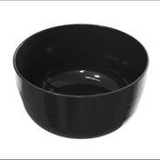 A glossy, empty black cast aluminum bowl with a smooth surface and slight horizontal ridges near its base is shown against a plain white background. The bowl is round, deep, and has a shiny, reflective finish.