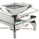 A shiny, stainless steel TableCraft chafing dish with a dome lid, rectangular food pan, and curved legs. A small, dishwasher safe side tray serves as a replacement spoon rest, attached to the front. The overall design is modern and reflective.
