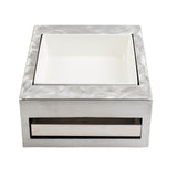 A square, metallic napkin holder from TableCraft Products features a brushed silver surface and a white, removable ceramic insert. With its modern, minimalist half size design, it offers clean lines and a polished appearance.