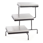 A 3-tiered metal display stand with rectangular, silver-colored cooling plates for shelves and black metal legs, each tier offset at different heights and positions, designed for showcasing items in a stepped arrangement.
