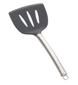 A slotted serving spatula with a black, wide, silicone head featuring three elongated holes and a curved stainless steel handle ending in a metal hanging loop. The spatula is set against a plain white background.