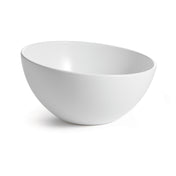 A white, round Sierra Collection Bowl with smooth, clean lines sits on a white surface. The bowl is empty and angled slightly to the left, casting a faint shadow on the right. A plain, bright background emphasizes the bowl’s shape and simplicity.