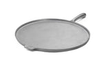 A flat, round, cast iron griddle with a slightly raised edge, a short side handle, and a smaller helper tab on the opposite side—ideal as a pizza pan—shown on a white background.