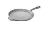 A gray, round pizza pan with a flat surface, small pouring spout, and long handle, set against a white background. Sturdy and heavy, this griddle pan is also dishwasher safe for easy cleaning.