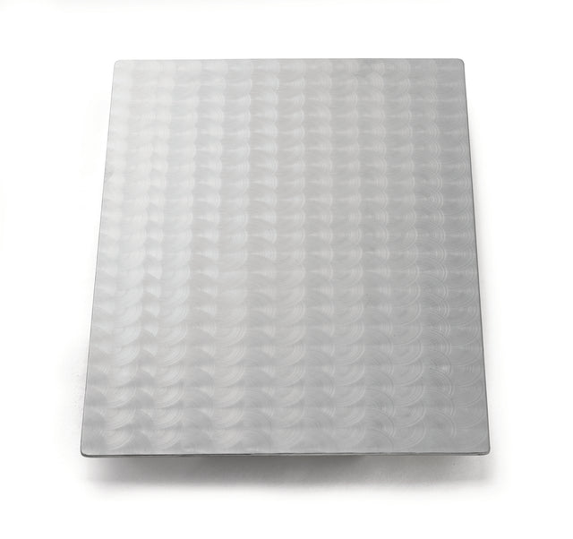 A rectangular sheet of Duracoat coated cast aluminum with a repeating circular swirl pattern covers the surface. The light gray, reflective metal is dishwasher safe and placed on a plain white background with soft shadows around the edges.