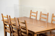 A wooden dining table with six matching chairs features TableCraft Products’ acrylic safety shield partitions, dividing the seating areas for added cafeteria safety and social distancing.
