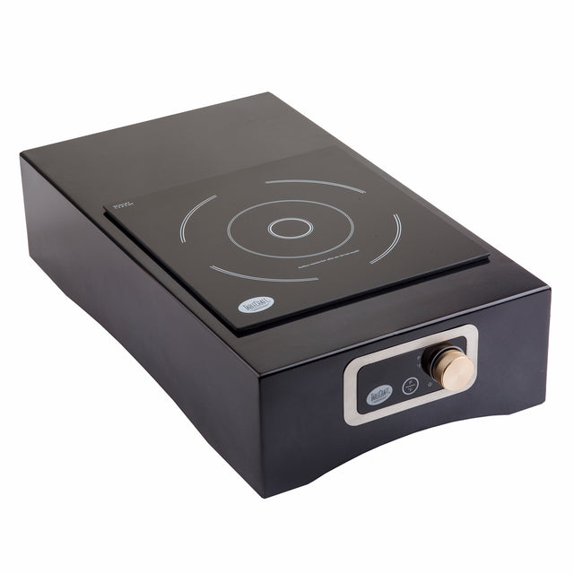 A modern black Induction Station cooktop with a single burner and a circular cooking zone. It features a digital display control panel and a round silver knob on the front, set against a slightly raised, rectangular base.