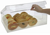 A hand lifts the clear lid of a BPA Free acrylic display bin containing two neat rows of assorted bagels, including plain, seeded, and poppy seed varieties. The bagels are arranged upright inside the transparent bakery case.