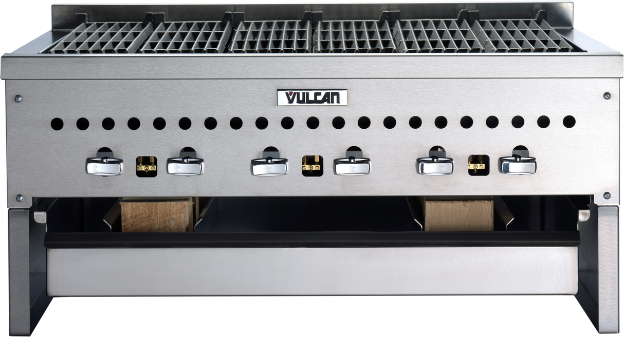 A stainless steel commercial grill with six black and silver control knobs, labeled “Vulcan,” features a metal grate on top and an open Wood Assist Smoker Base below containing two pieces of wood for convenient smoking.