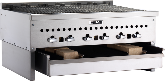 A stainless steel Vulcan commercial charbroiler with five control knobs, a grill on top, ventilation holes, and two lower drawers—featuring a Wood Assist Smoker Base with wooden blocks inside. The background is plain and white.