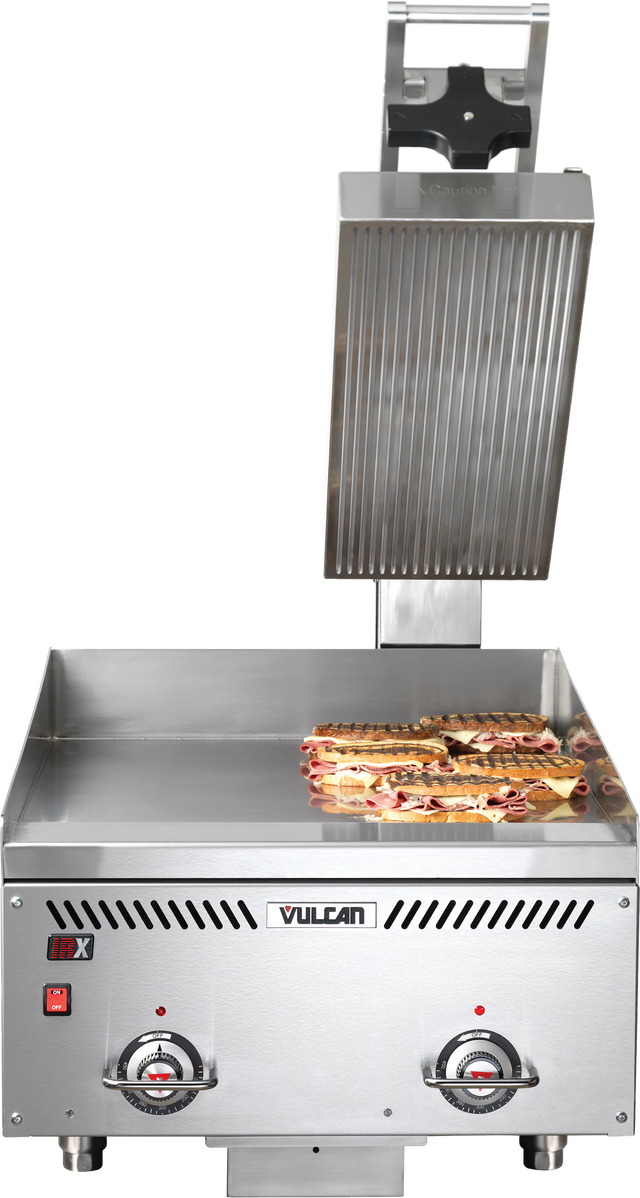 A commercial Vulcan sandwich press with an open top plate and thermostatic control, grilling several panini sandwiches on the flat bottom grill plate. The stainless steel machine features two control dials and indicator lights on the front panel.