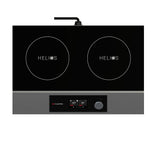 A modern black and silver portable induction cooktop with a double hob features two circular burners labeled “HELIOS.” Below, a control panel with digital displays, a knob, and buttons sits above the visible “CookTek” brand. The cooktop is plugged in at the back.