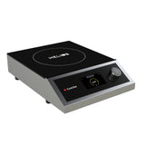 A modern portable induction cooktop with a sleek black glass surface, digital display, single control knob, and CookTek branding. The countertop appliance features a white circle with “HELIOS” text at the center, metal sides, and four small feet.
