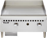 The Vulcan VCRG24-M is a stainless steel 24" countertop gas griddle with two control knobs, smooth flat-top surface, short metal legs, small ventilation holes above the knobs, and a grease tray underneath on the left side.