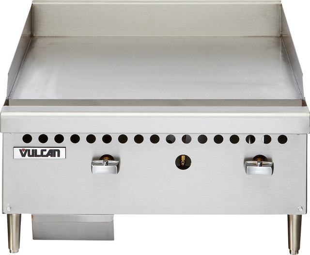 The Vulcan VCRG24-M is a stainless steel 24" countertop gas griddle with two control knobs, smooth flat-top surface, short metal legs, small ventilation holes above the knobs, and a grease tray underneath on the left side.